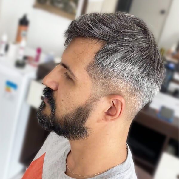 A man with grey hair and beard in front of a refrigerator.